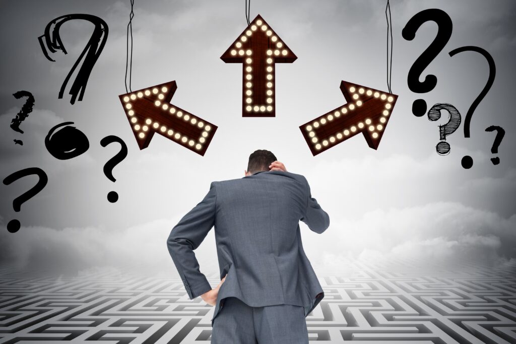 Confused businessman standing in front of multiple directional arrows and question marks, symbolizing decision-making uncertainty.