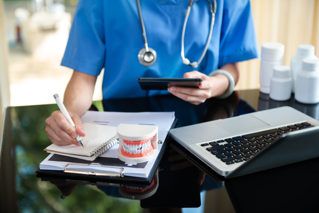 concentrated-dentist-sitting-table-with-jaw-samples-tooth-model-working-with-tablet-laptop-dental-office-professional-dental-clinic