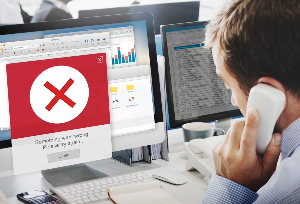 A man on the phone looks at a computer screen displaying an error message with a red X and the text "Something went wrong. Please try again.