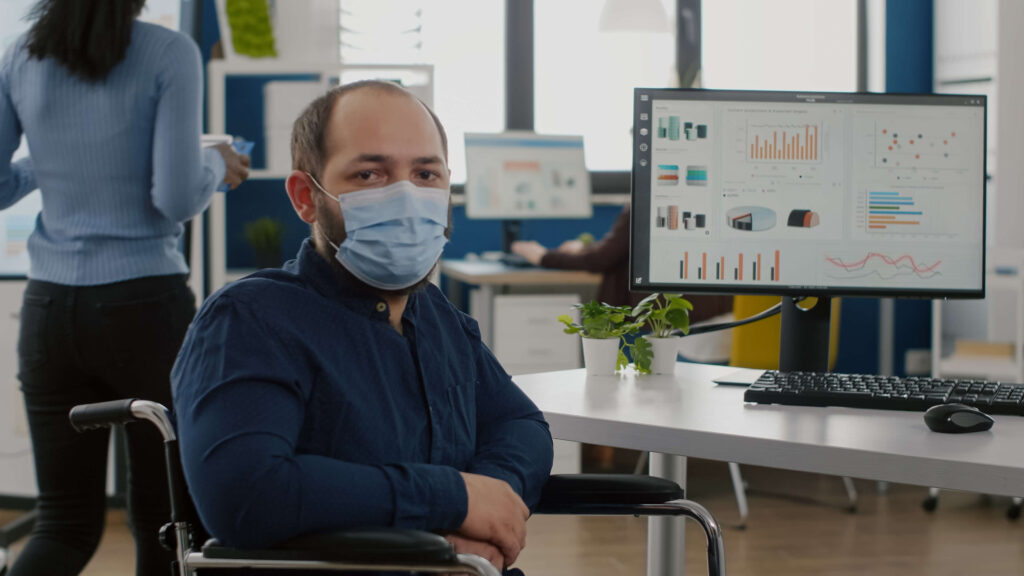 employee-with-disabilities-invalid-handicapped-paralized-with-face-mask-against-coronavirus-looking-camera-sitting-immobilized-wheelchair-business-office-room-working-financial-project