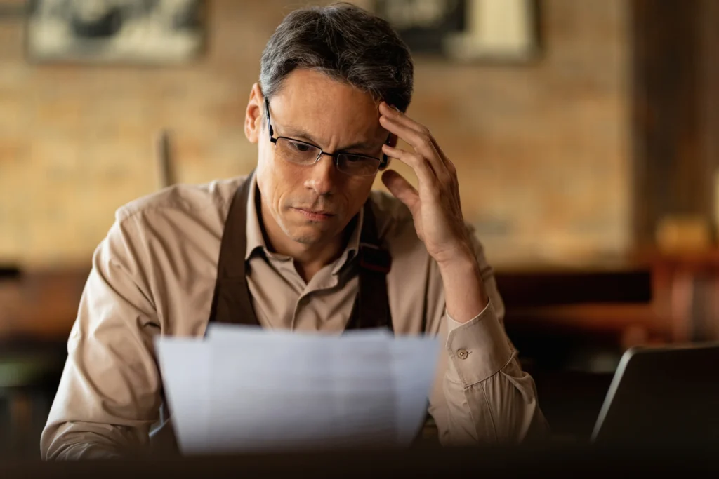 distraught-small-business-owner-reading-reports-while-going-through-paperwork-bar