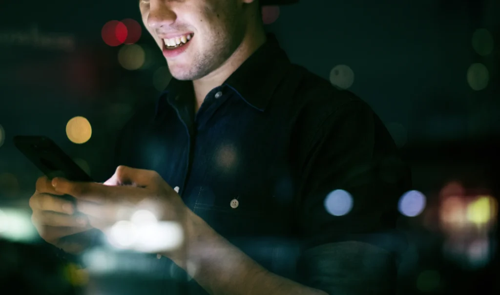 happy-young-adult-male-using-smartphone-night-cityscape